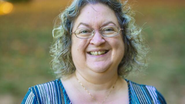 Laura Steakin smiles while standing outside and wearing a blue striped shirt.