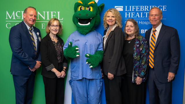Group of people in suits stand with the Green Terror mascot with McDaniel College and Lifebridge Health Logos behind them