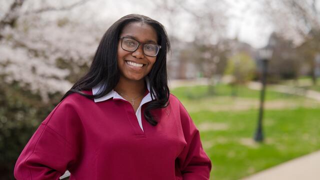 A female student in glasses smiles in front of flowering trees on the McDaniel campus.