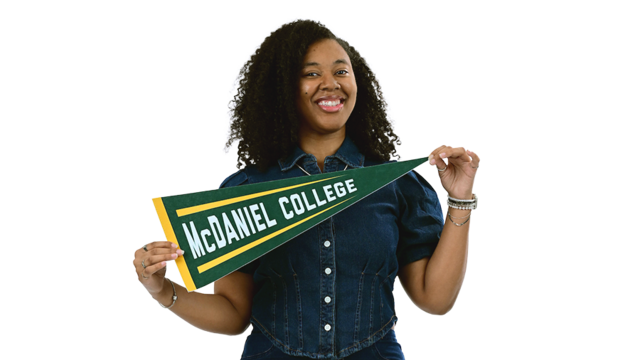A female student wearing a denim outfit poses with a McDaniel College pennant.