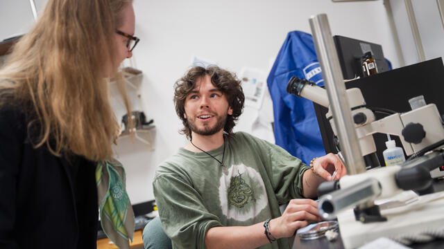 A male student shows his work with a microscope in the lab.