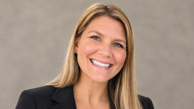 A blonde woman smiles in a black blazer and a white shirt.