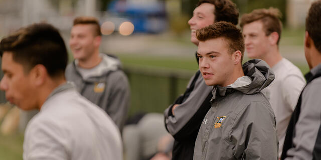 Men's soccer players on the sidelines.