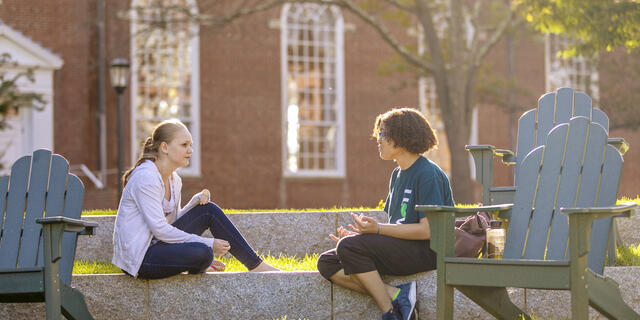 Students in conversation sitting near outdoor chairs.