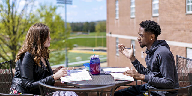 Two students in conversation sitting at outdoor table.