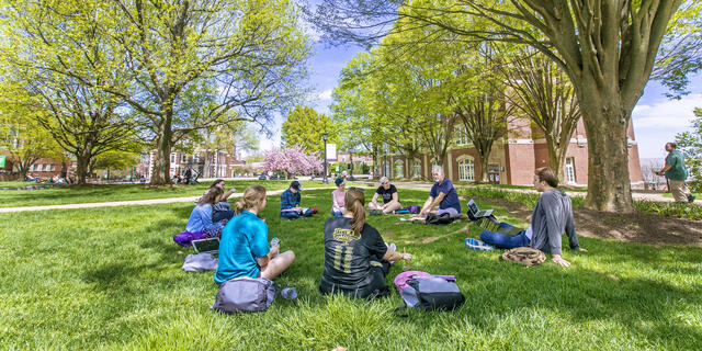 Professor lecturing class outdoors sitting on campus lawn.