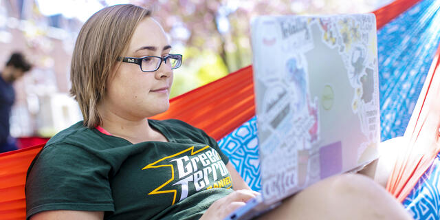 Student on computer in hammock on campus.