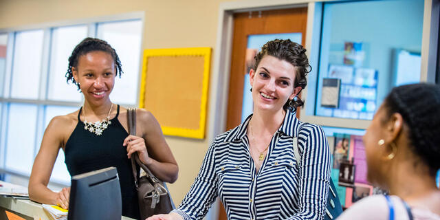 Grad students interacting at desk counter.