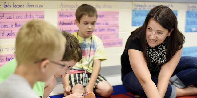 Student interacting with elementary school children on carpet.