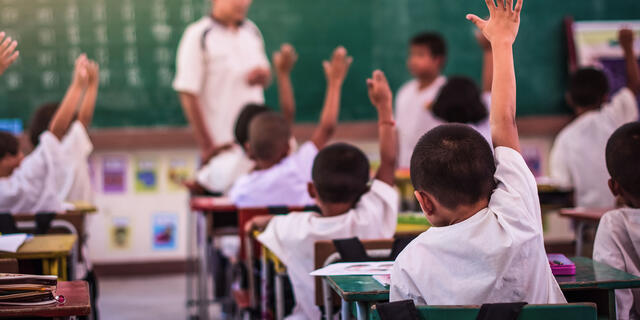Elementary students raising their hands in classroom.