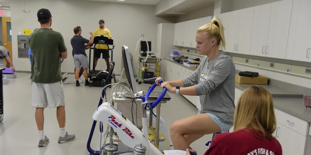 Student riding stationary bike in exercise classroom.