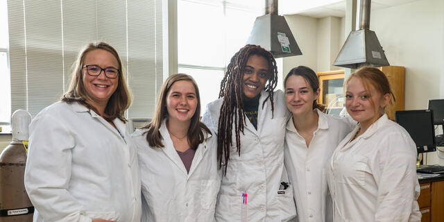 Professor Stephanie Homan poses with three students in the Chemistry lab.