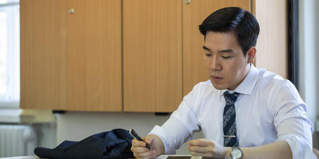 A student in a white button-down short looks at papers on a desk.