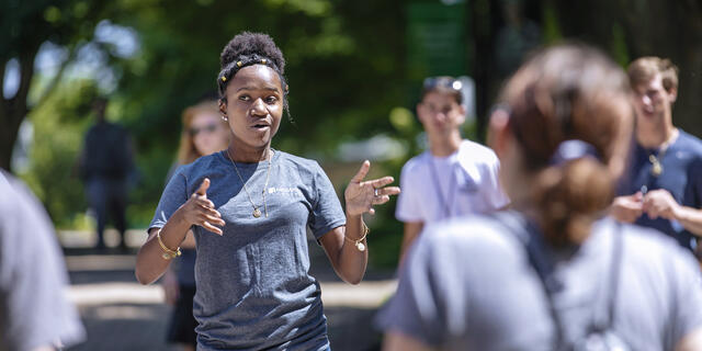 A students speaks to a group of other students outside on campus.