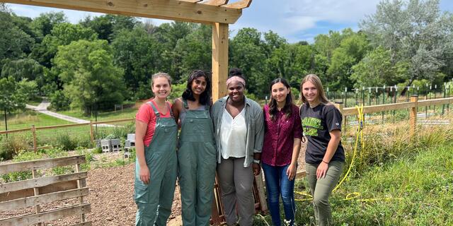 Four students pose with professor Elly Engle in front of a vegetable garden at the McDaniel Environmental Center.
