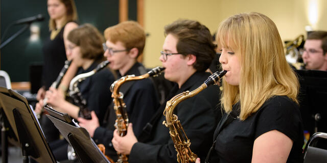 Students sit in a row playing saxophones.