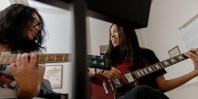 Two students hold guitars while smiling at each other.