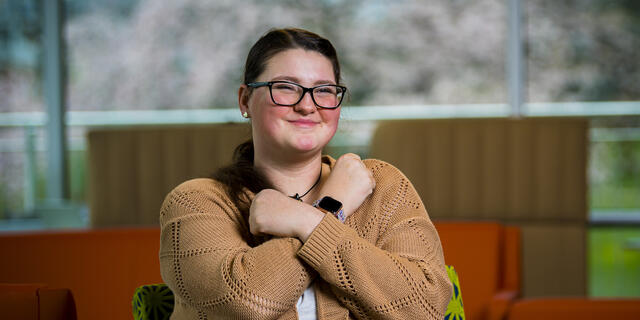 A student holds a pose in American Sign Language while sitting in the campus student center.