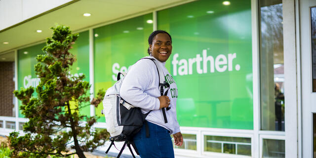 A student smiles to the side while walking with a backpack on their shoulder.