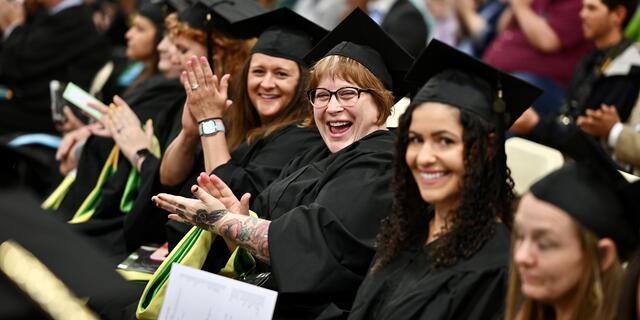 Group of students in commencement regalia sit in chairs