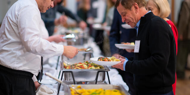 Event attendee is served food by a catering staff member at a buffet style food line.