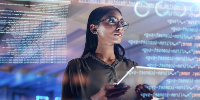 A woman with long, straight hair and glasses holds a tablet and looks at a screen of computer code.