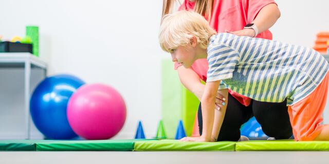 Young boy exercising with female physical therapist during therapy session. Child occupational physical therapy. Bilateral coordination.